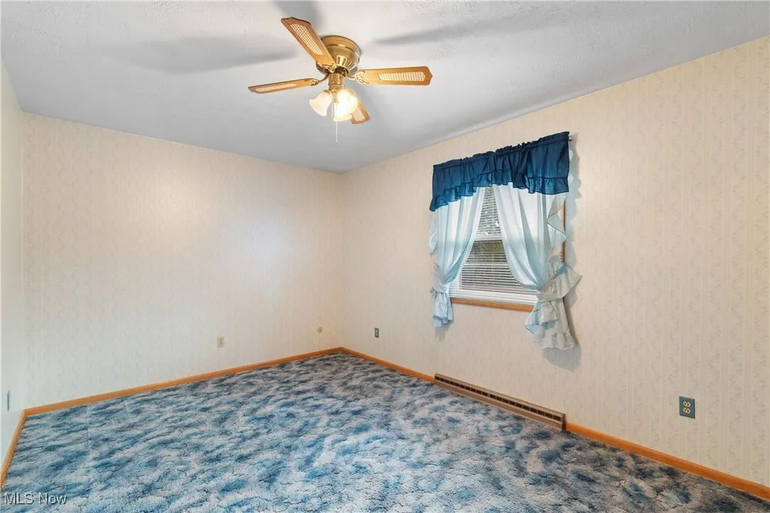 Empty room with a baseboard heating unit, wallpapered walls, a textured ceiling, ceiling fan, and carpet floors
