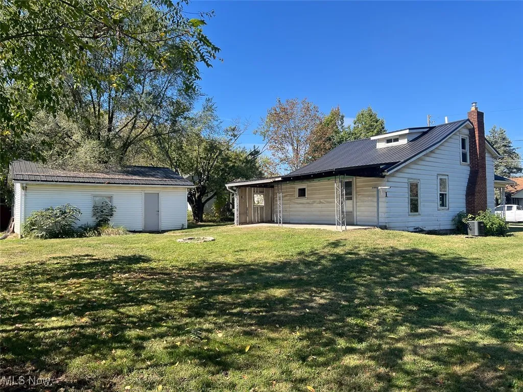 Back of property with a chimney, a lawn, and a metal roof
