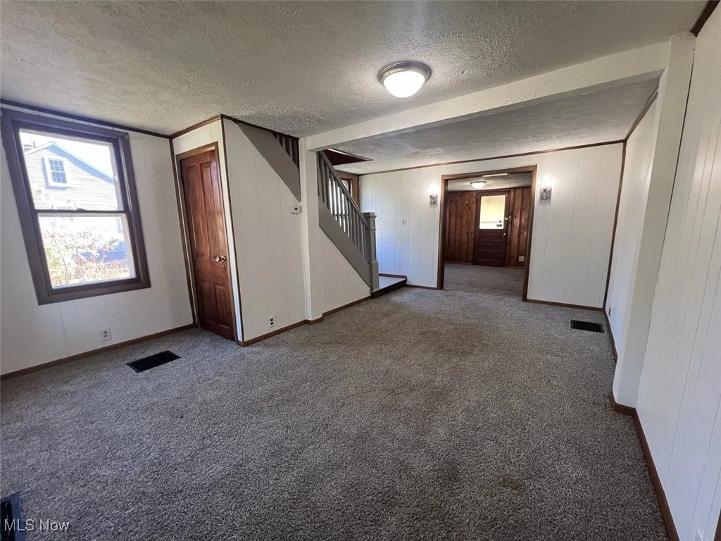 Living room with a textured ceiling, dark carpet, healthy amount of natural light, wood walls, and stairs