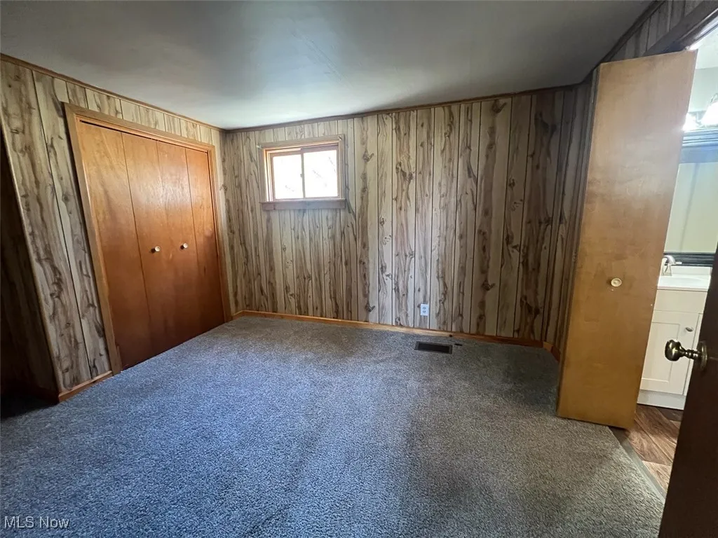 Unfurnished bedroom with wood walls, a closet, and carpet