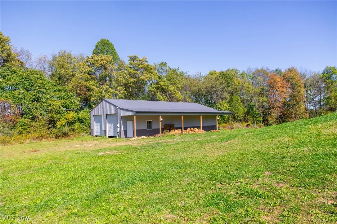 Rear view of house featuring a lawn, an outdoor structure, a garage, and a wooded view