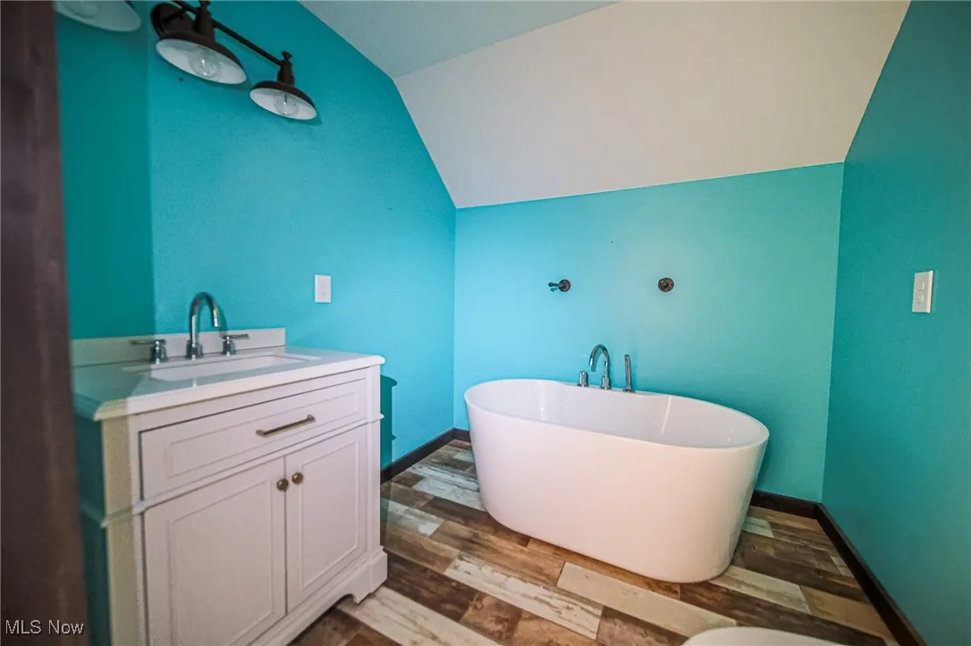 Full bathroom with a soaking tub, vanity, dark wood-type flooring, and vaulted ceiling