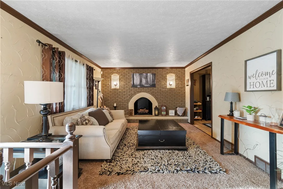 Living area with a textured wall, a textured ceiling, carpet flooring, a fireplace, and ornamental molding
