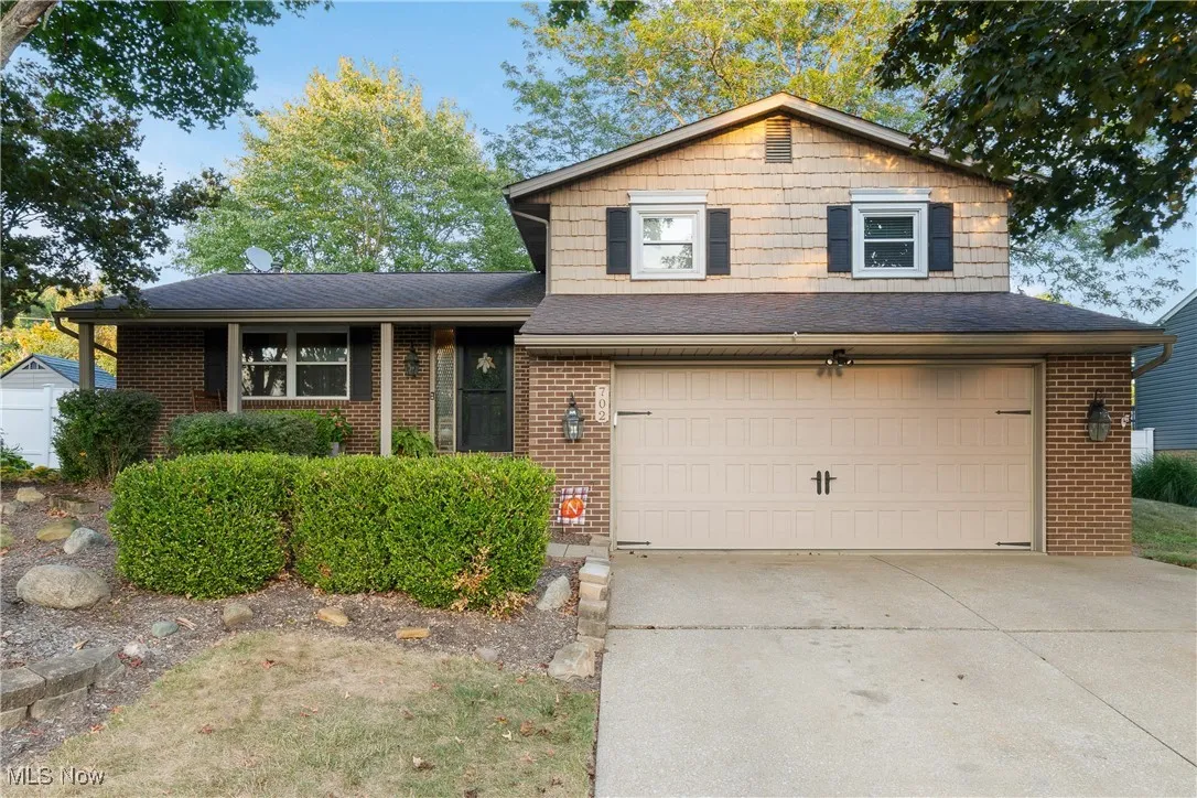 Split level home featuring driveway, a garage, a shingled roof, and brick siding
