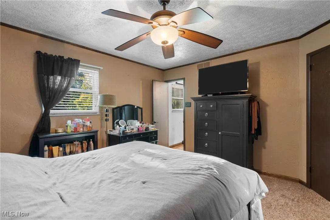 Bedroom with a textured wall, crown molding, a textured ceiling, light carpet, and ceiling fan