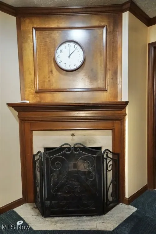 Detailed view of master bedroom fireplace with flush hearth, a textured ceiling, crown molding, and carpet