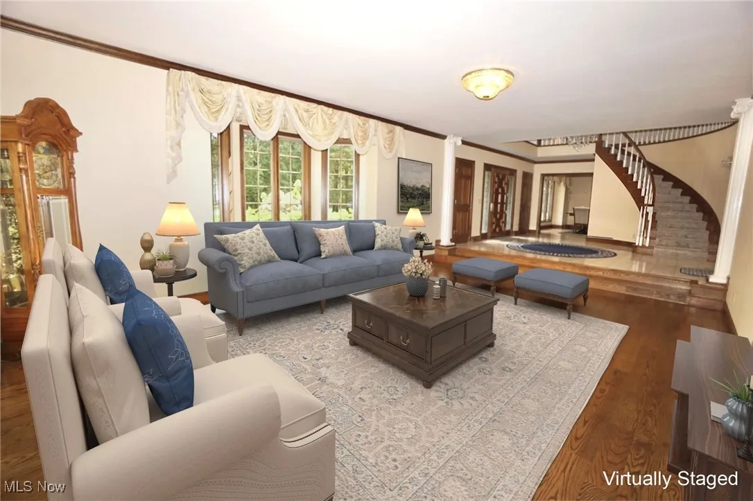 Living room with wood finished floors, ornamental molding, and stairway