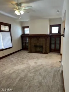 Unfurnished living room featuring carpet flooring, plenty of natural light, a brick fireplace, and a ceiling fan