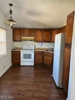 Kitchen featuring white appliances, brown cabinetry, dark wood finished floors, light countertops, and decorative light fixtures