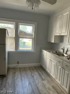 Kitchen with freestanding refrigerator, white cabinetry, light wood-type flooring, and light countertops