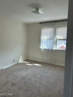 Carpeted spare room featuring baseboards