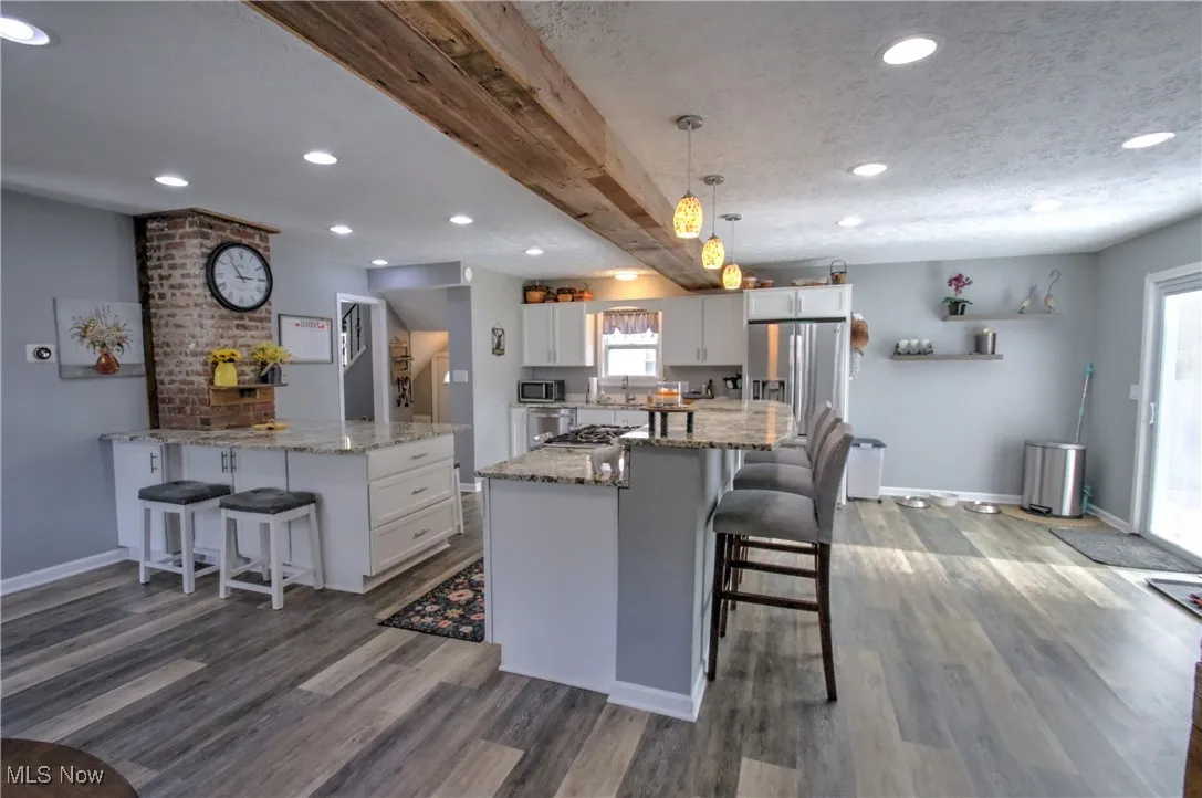 Kitchen featuring a kitchen breakfast bar, beamed ceiling, decorative light fixtures, light granite countertops, and recessed lighting