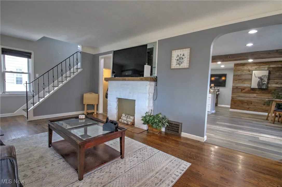 Living area with stairway, dark wood-type flooring, wood walls, a decorative fireplace, and arched walkways