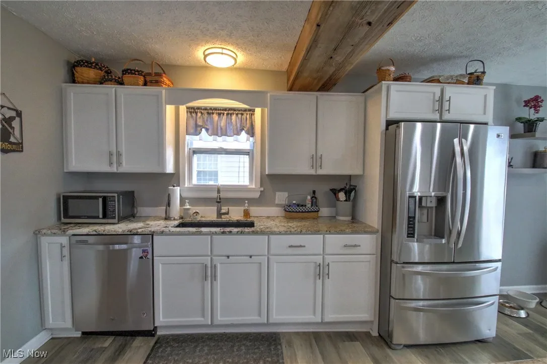 Kitchen featuring stainless steel appliances, a textured ceiling, white cabinets, light wood-style flooring, and light granite counters