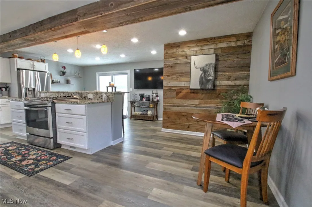Kitchen with wooden walls, white cabinetry, pendant lighting, stainless steel appliances, and light granite counters
