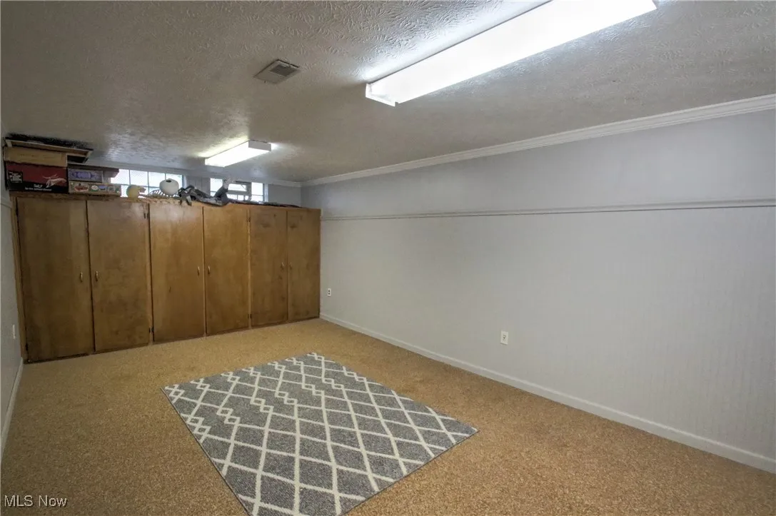 Basement with a textured ceiling, light nature stone flooring, and crown molding