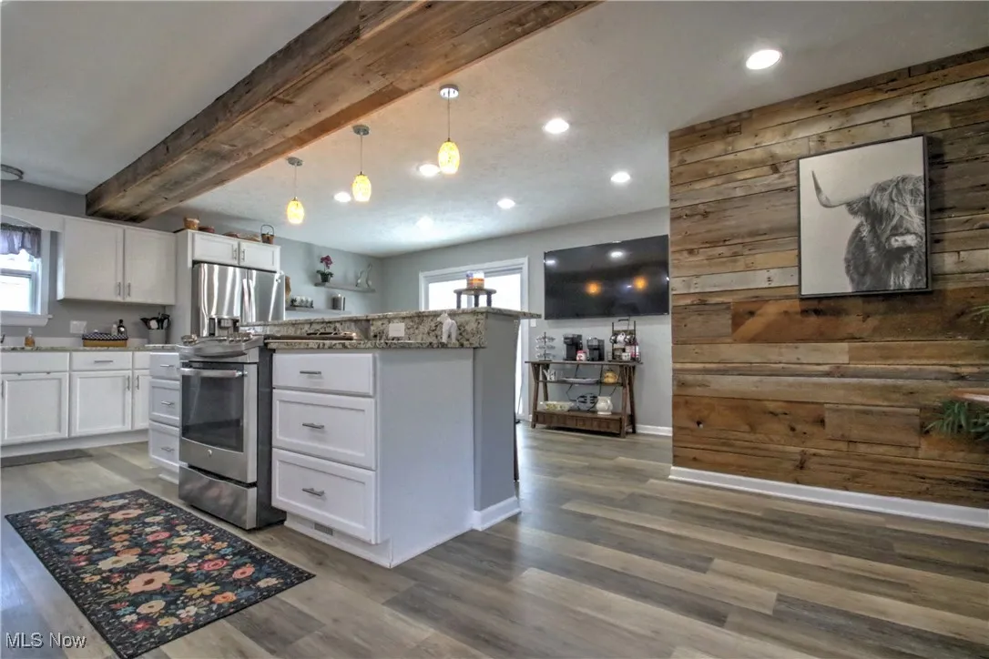 Kitchen with beamed ceiling, wooden walls, white cabinetry, stainless steel fridge, and light wood-type flooring