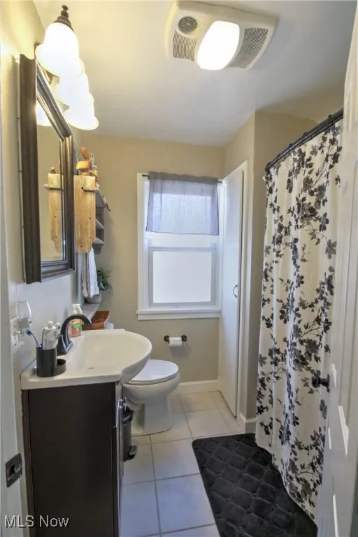 Full bathroom with vanity, light tile patterned floors, and curtained shower