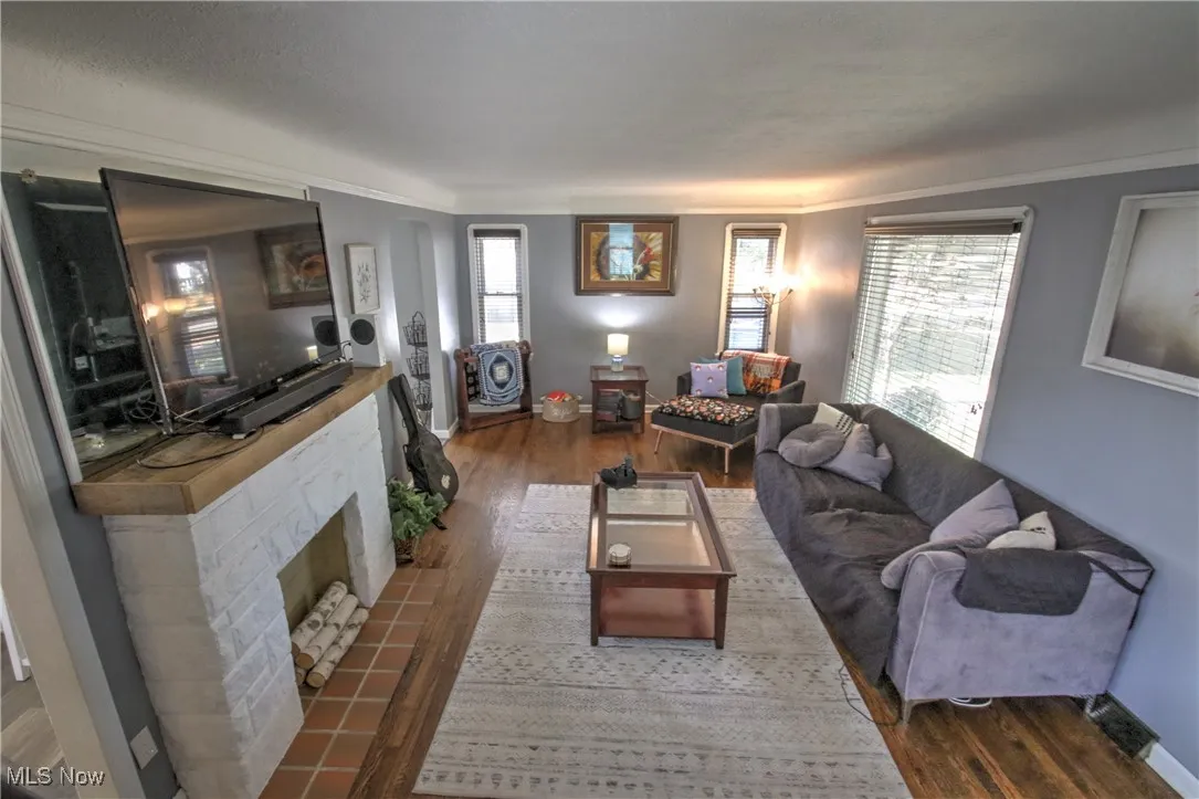 Living area featuring healthy amount of natural light, dark wood-type flooring, crown molding, and a beautiful decorative fireplace with flush hearth