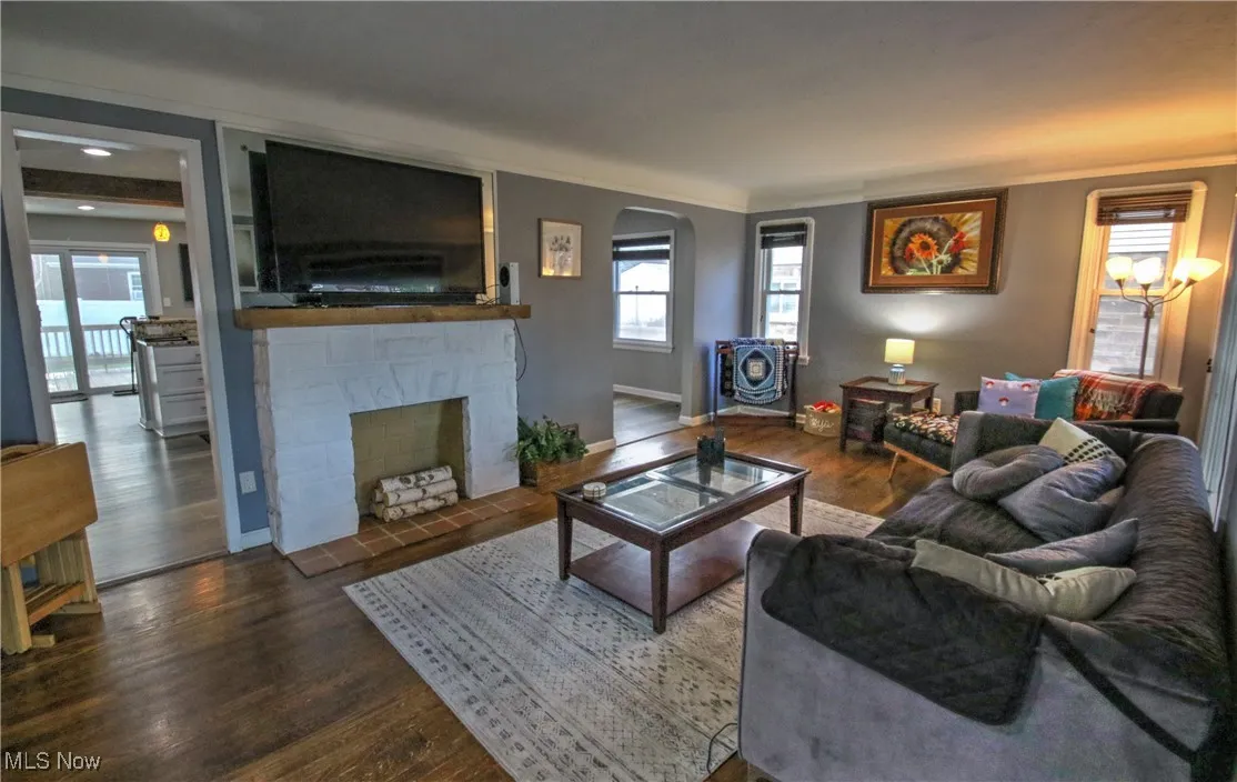 Living room with wood finished floors, a beautiful decorative fireplace, and ornamental molding