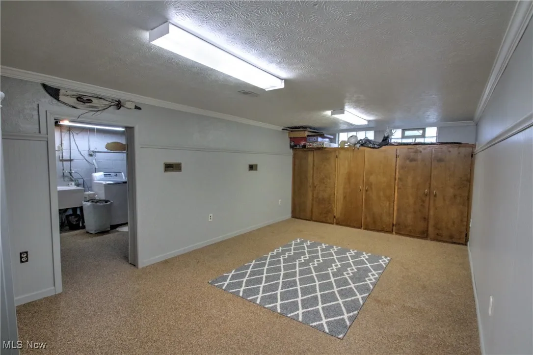 Below grade area featuring crown molding, washer / clothes dryer, a textured ceiling, and light nature stone flooring