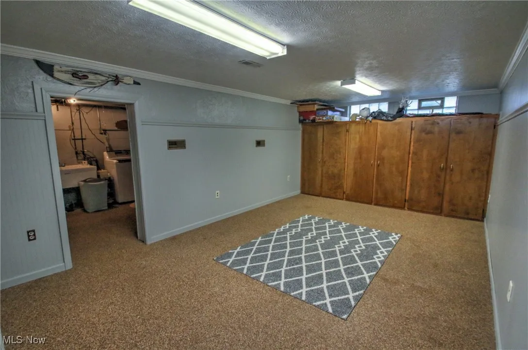 Below grade area featuring crown molding, a textured ceiling, light nature stone flooring, and washer / dryer