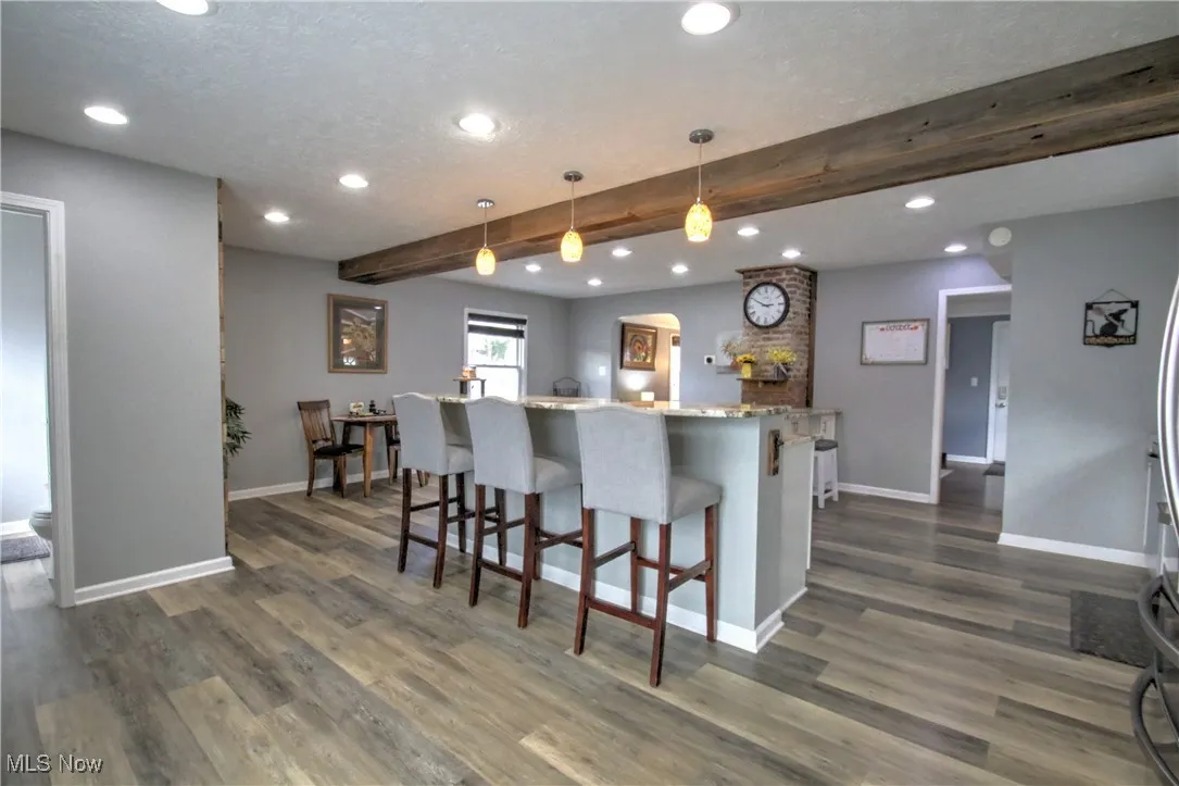Kitchen featuring beam ceiling, recessed lighting, a kitchen bar, light granite counters, and hanging light fixtures