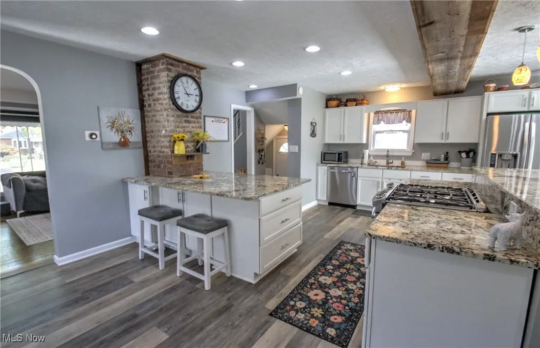 Kitchen featuring a kitchen bar, light granite counters, appliances with stainless steel finishes, dark wood-style floors, and recessed lighting