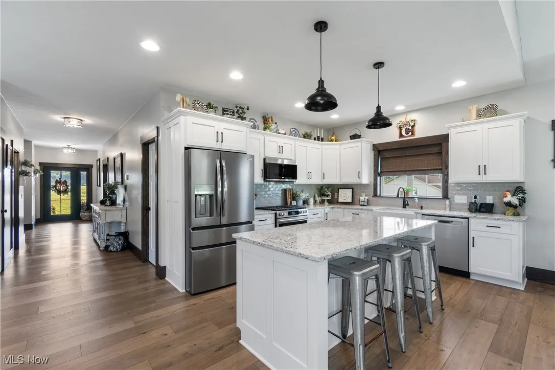 Kitchen with appliances with stainless steel finishes, white cabinetry, a kitchen bar, dark wood-style floors, and recessed lighting
