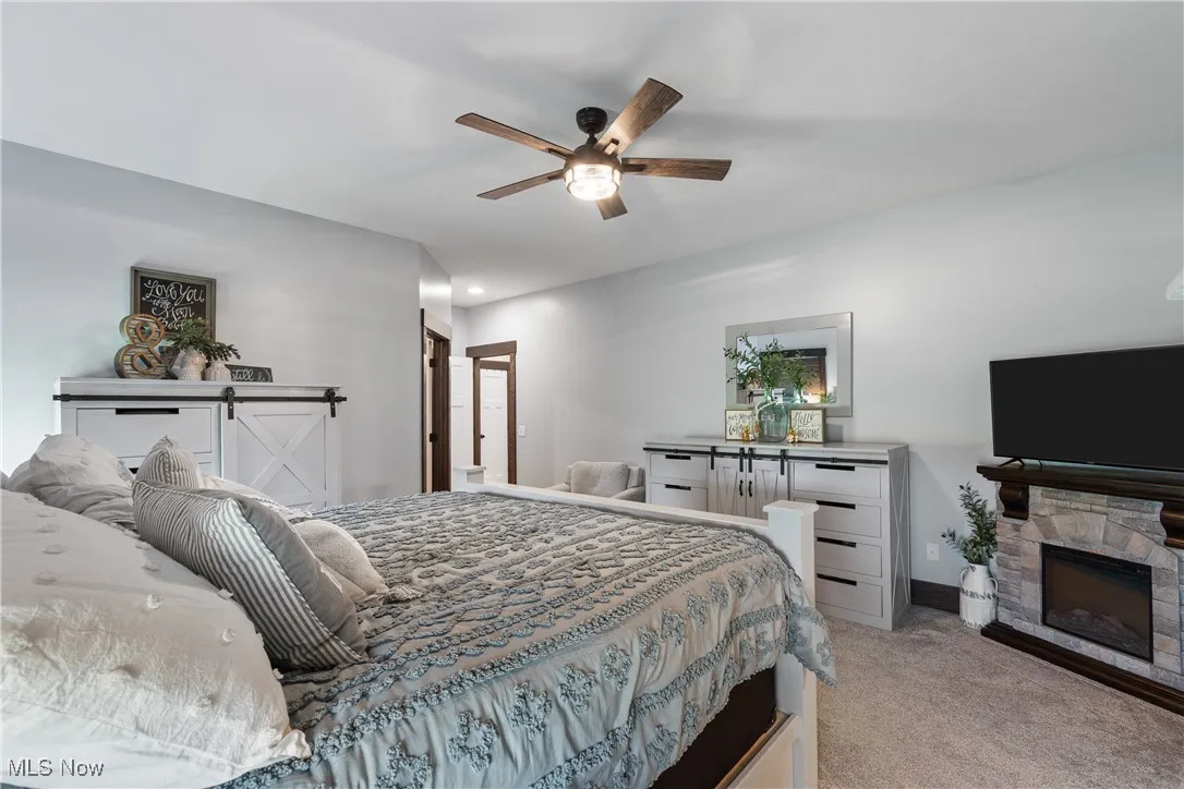 Bedroom featuring light colored carpet, a stone fireplace, and a ceiling fan