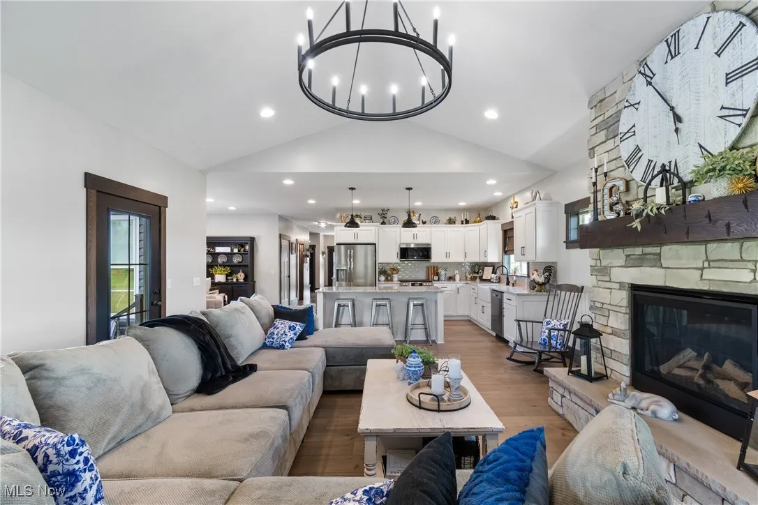 Living area featuring wood finished floors, a stone fireplace, lofted ceiling, and recessed lighting