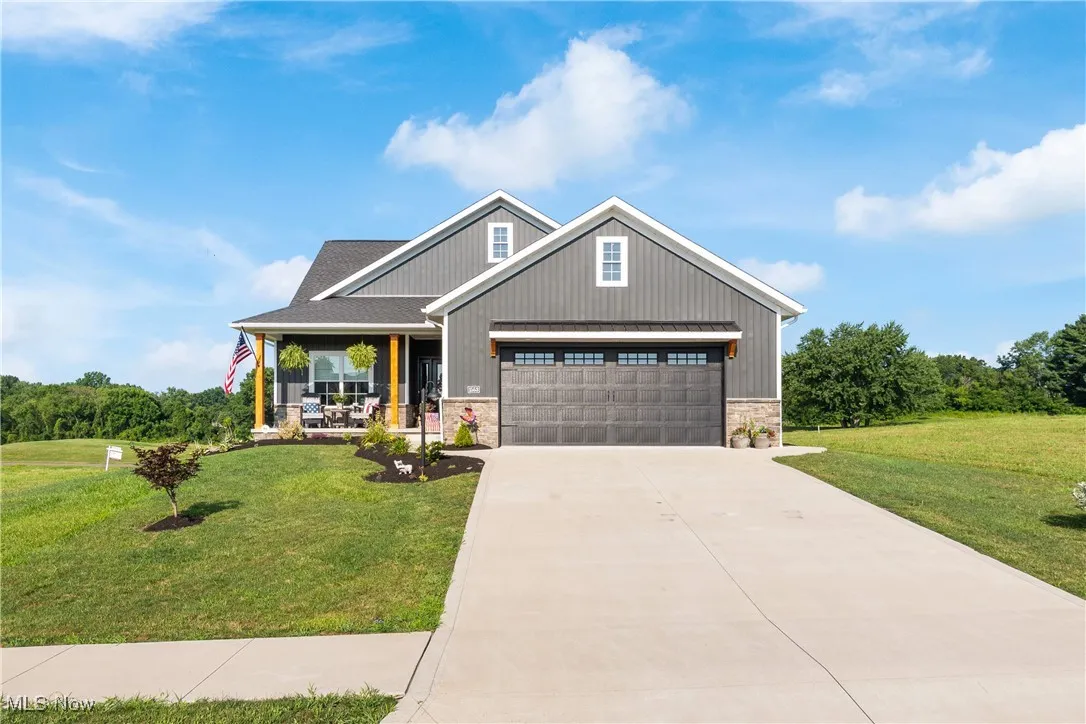 Craftsman-style house featuring covered porch, a front lawn, concrete driveway, and stone siding