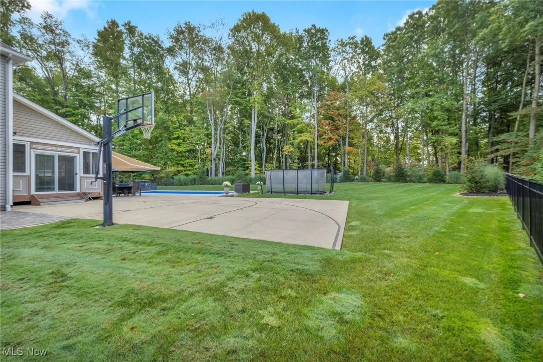 View of sport court with a patio, basketball court, view of scattered trees, and a sunroom