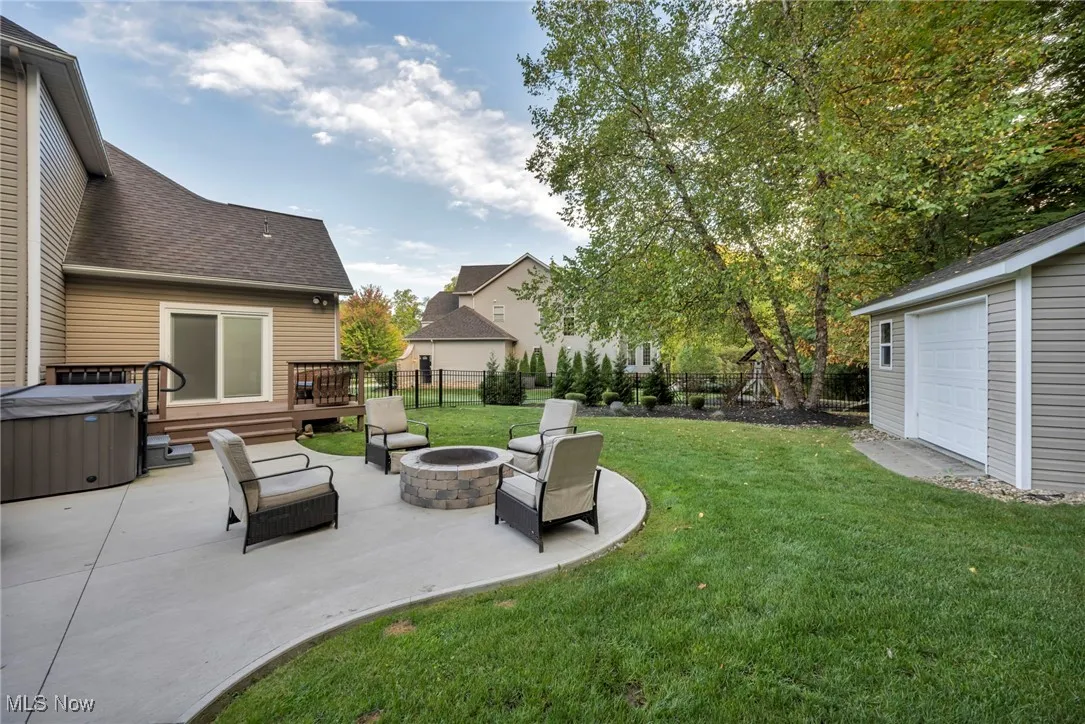 Fenced backyard featuring a fire pit, a patio area, a deck, a hot tub, and an outdoor structure