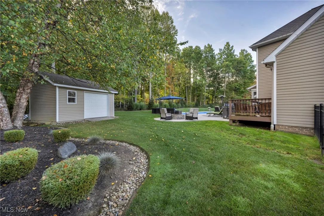 View of grassy yard featuring a patio area, an outdoor fire pit, a wooden deck, and an outbuilding