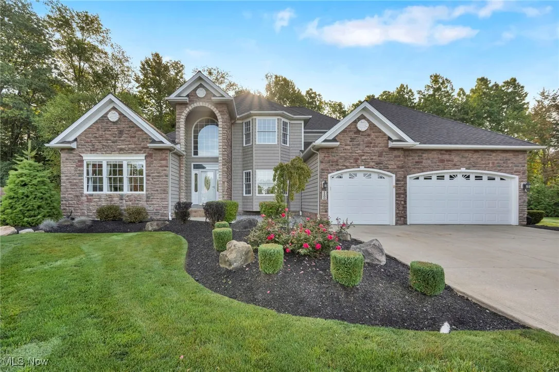 Traditional home with stone siding, driveway, a front lawn, a garage, and roof with shingles