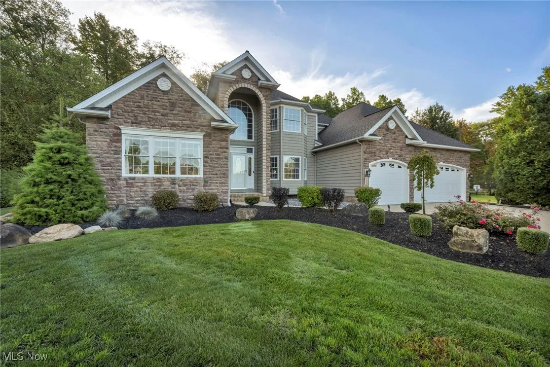 Traditional-style home featuring a front yard, a garage, and stone siding