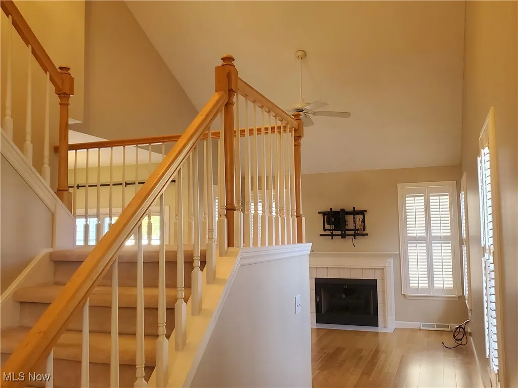 Staircase with wood finished floors, a tile fireplace, ceiling fan, and lofted ceiling