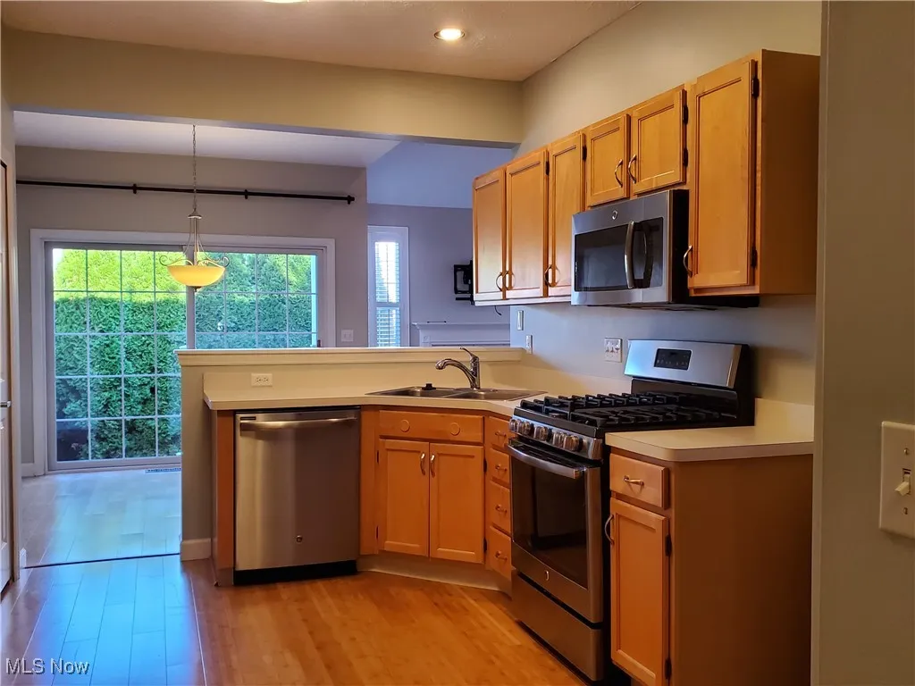 Kitchen with stainless steel appliances, hanging light fixtures, a peninsula, light wood-type flooring, and light countertops