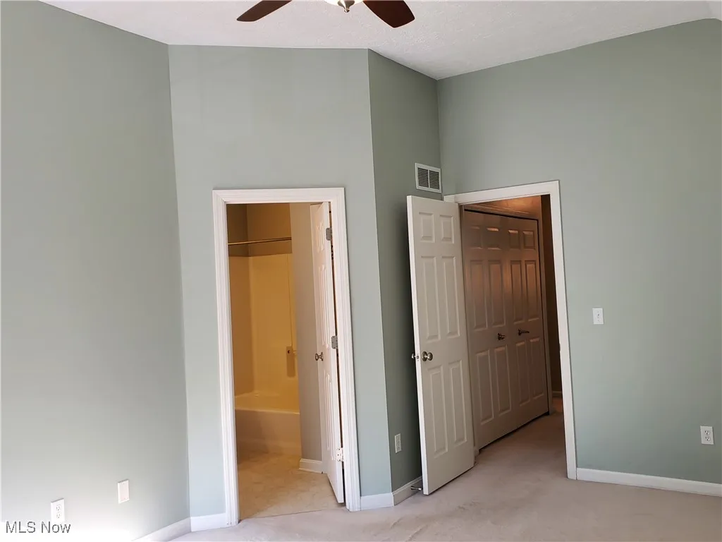 Unfurnished bedroom with light colored carpet, ensuite bathroom, ceiling fan, and a textured ceiling