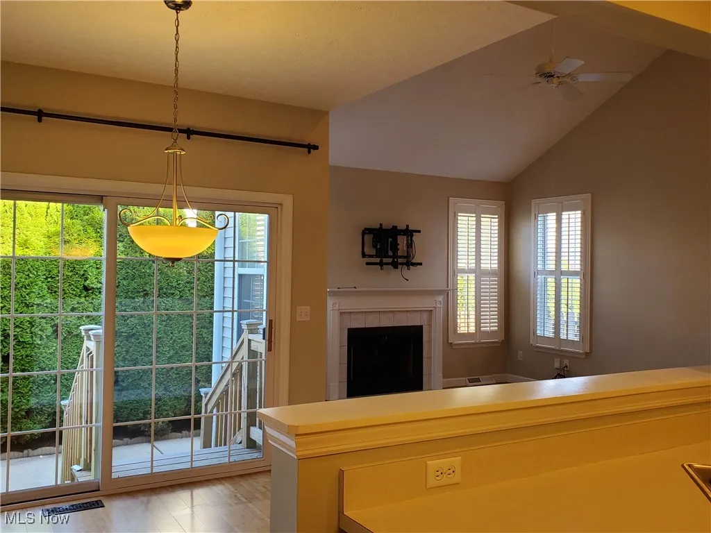 Living room featuring a tile fireplace, light wood-type flooring, lofted ceiling, and ceiling fan