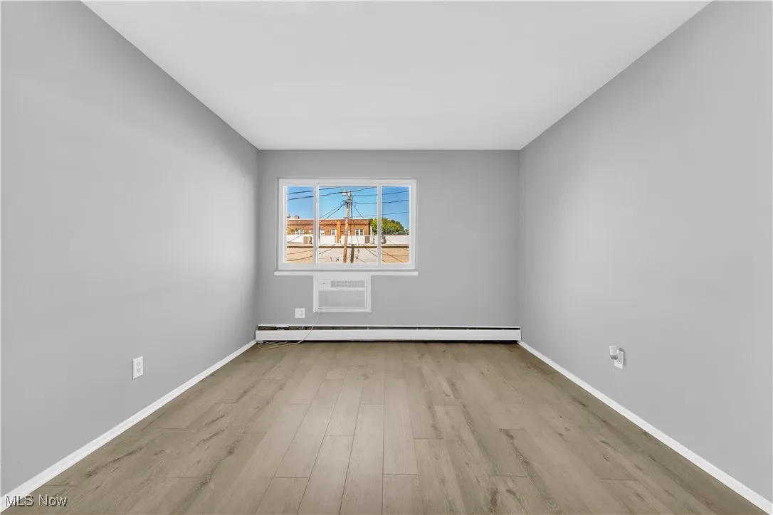Spare room featuring light wood-style flooring, an AC wall unit, and baseboard heating