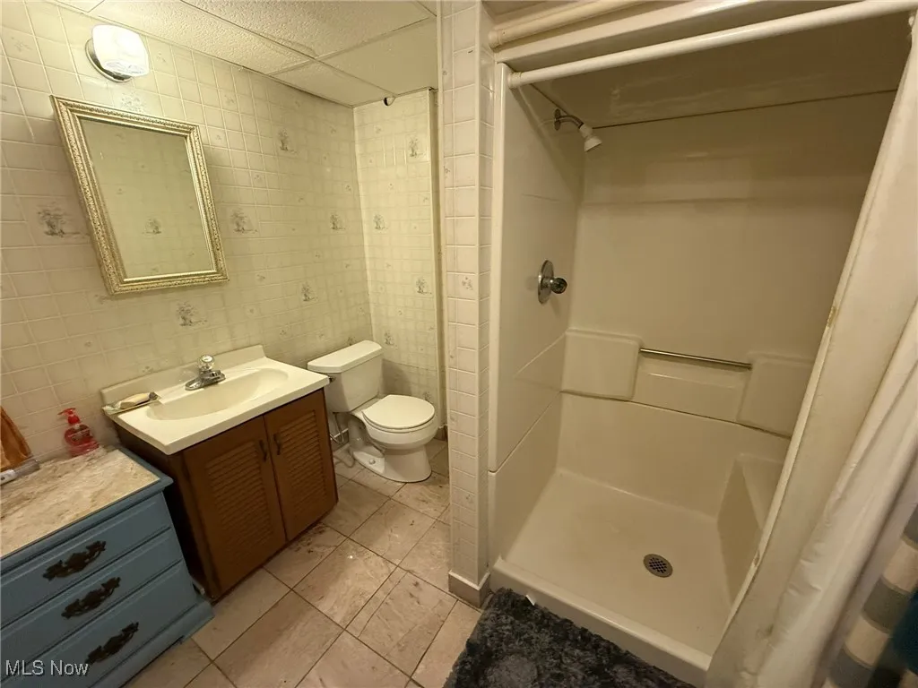 Full bath featuring a shower stall, vanity, tile walls, and light tile patterned floors