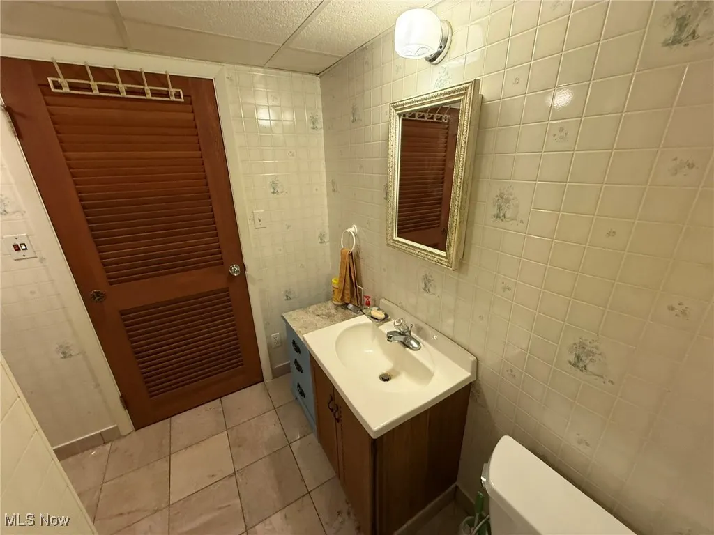Half bathroom with tile walls, vanity, light tile patterned floors, and a drop ceiling