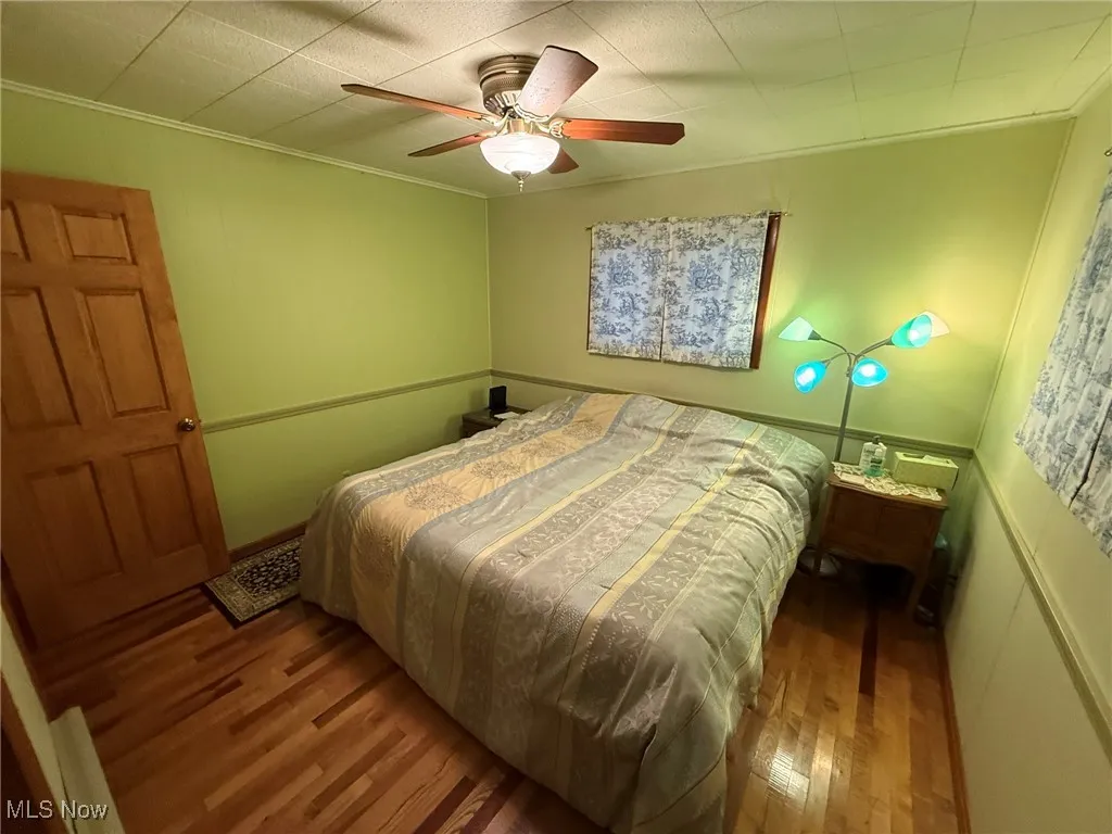 Bedroom with wood finished floors, a ceiling fan, and crown molding