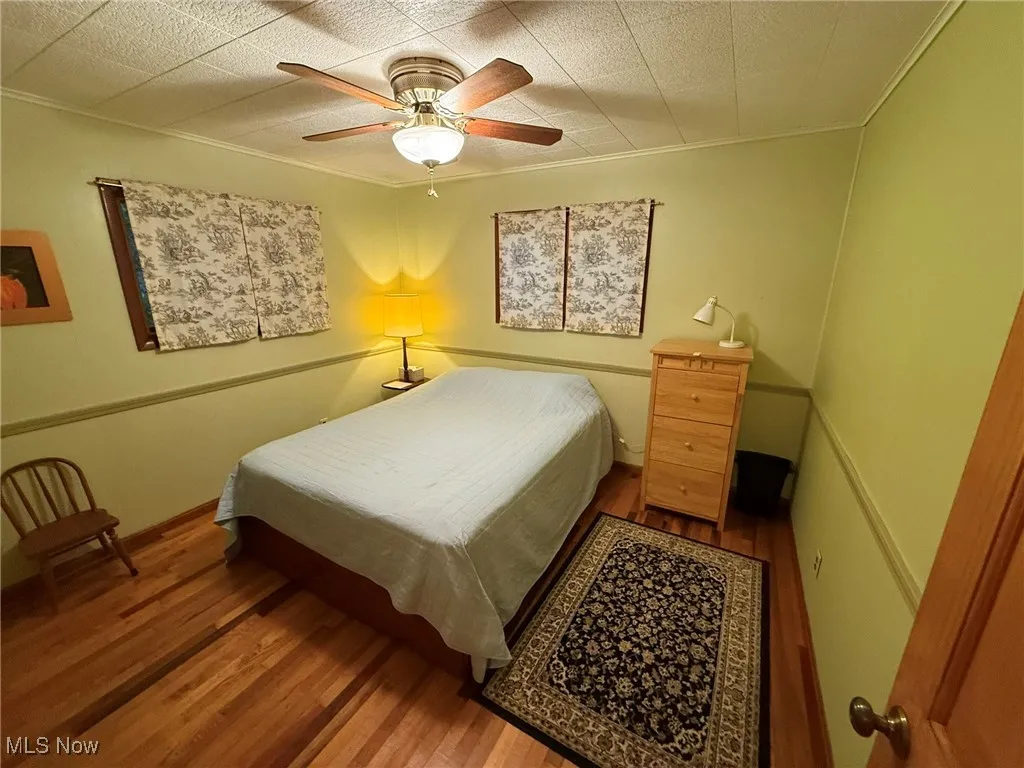Bedroom with a ceiling fan, wood finished floors, and ornamental molding
