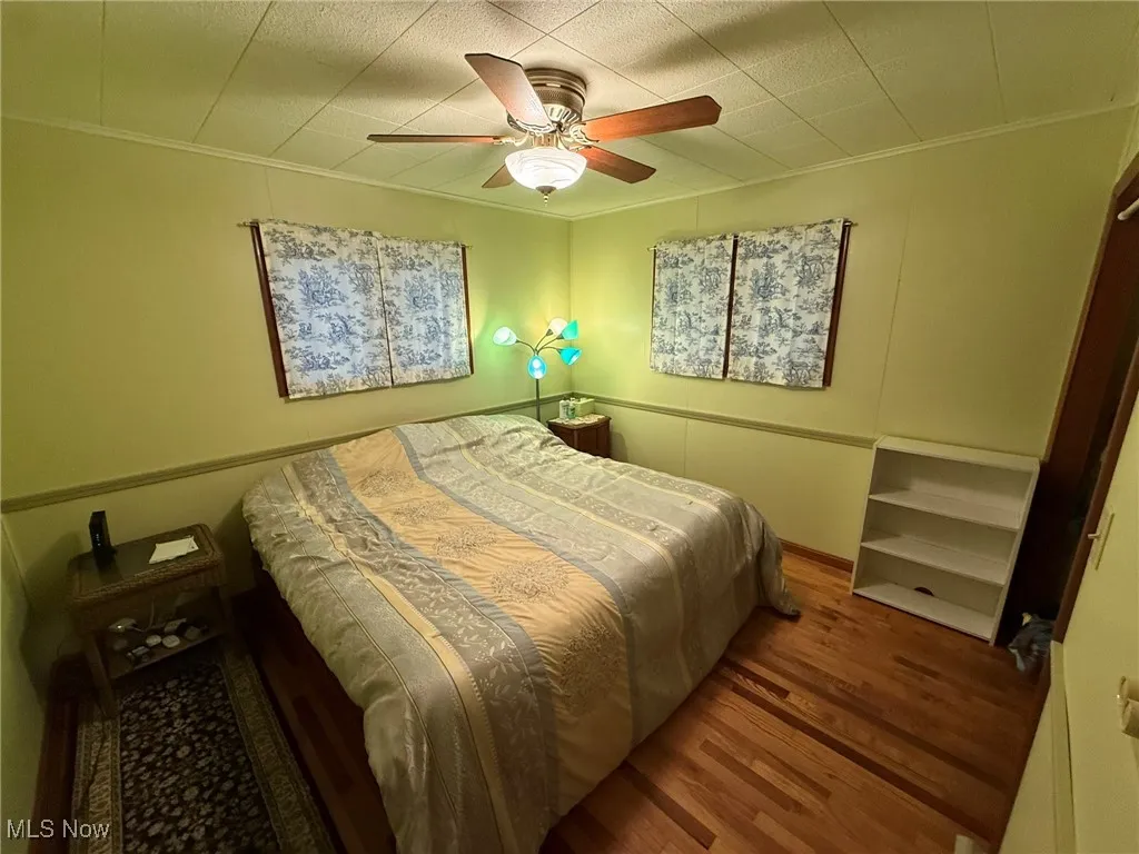 Bedroom with wood finished floors, crown molding, and a ceiling fan