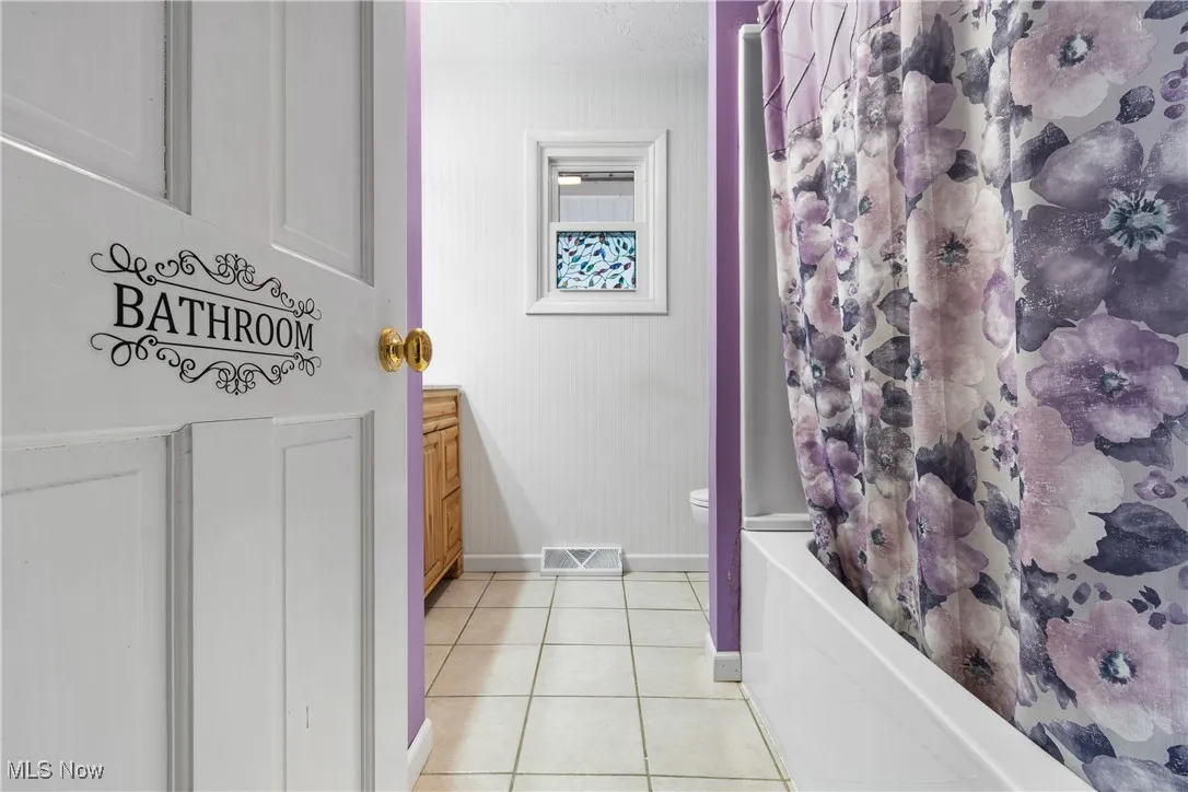 Bathroom with light tile patterned floors, vanity, and shower / bath combo with shower curtain