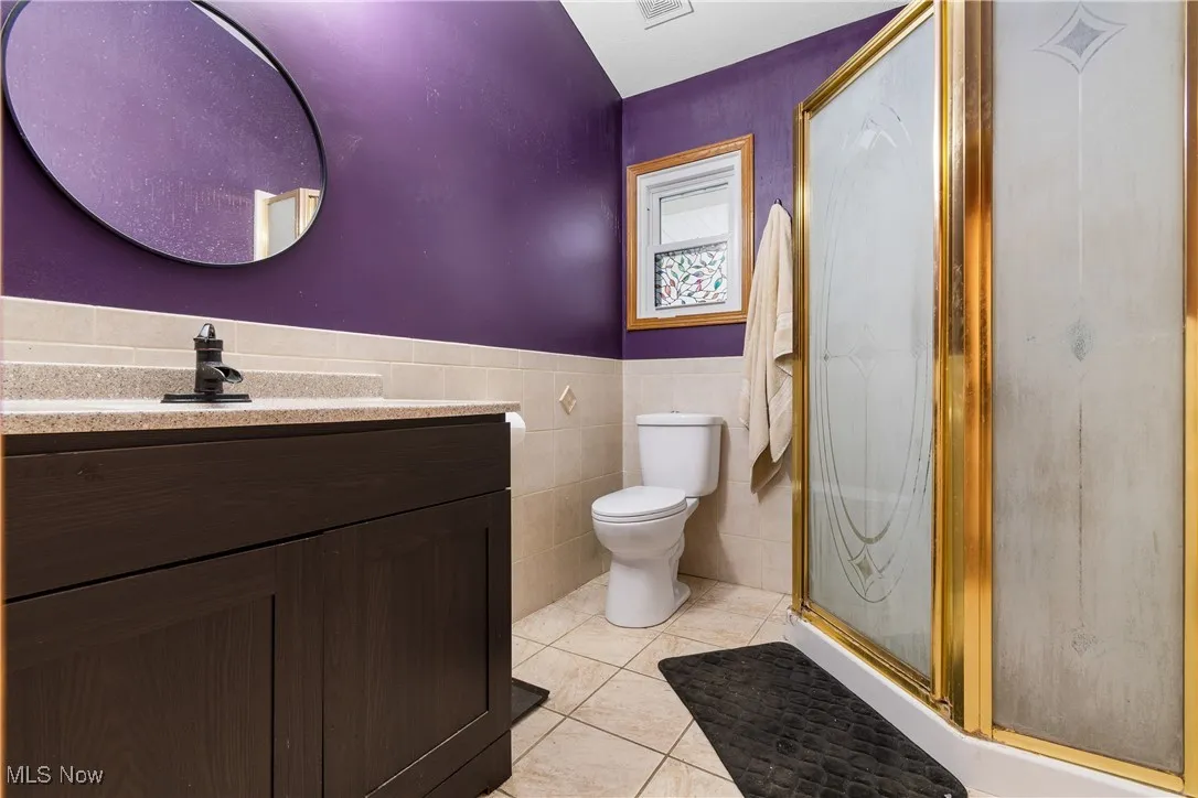 Full bath featuring vanity, tile walls, a shower stall, light tile patterned flooring, and wainscoting