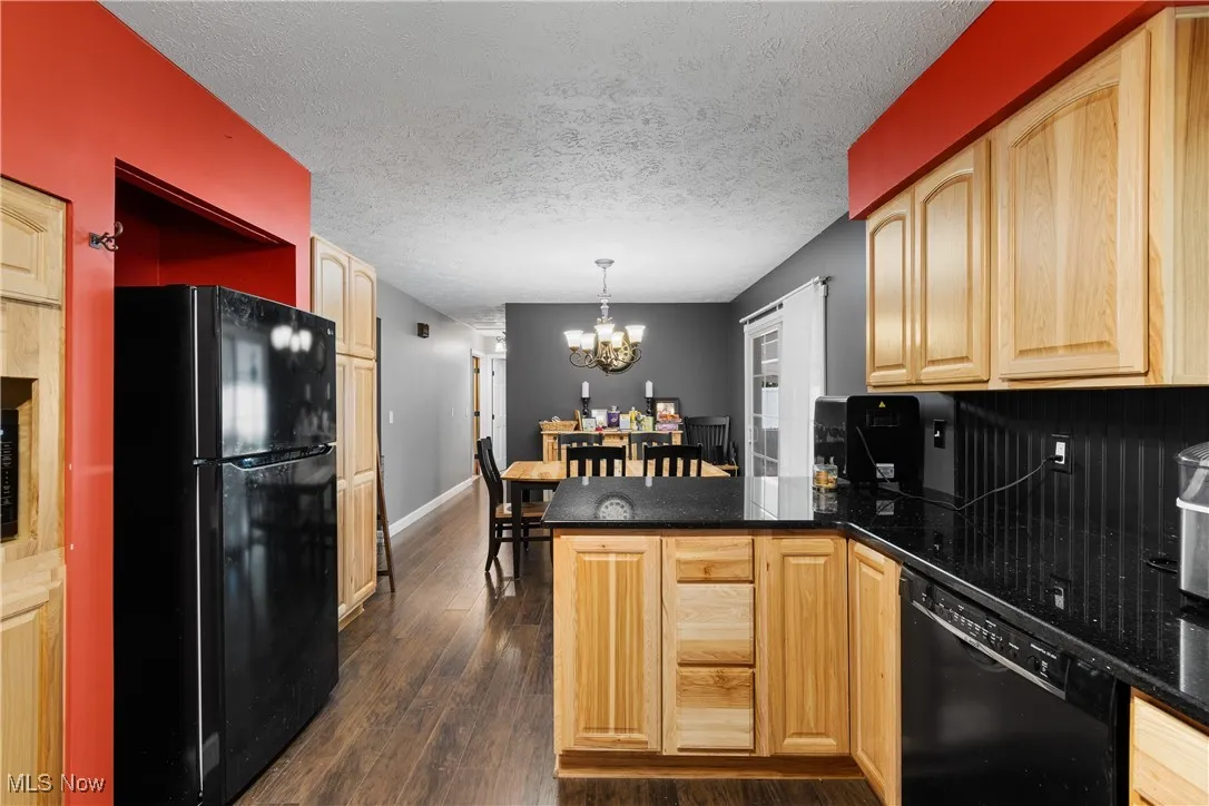 Kitchen with a peninsula, black appliances, decorative light fixtures, dark wood-style floors, and a chandelier